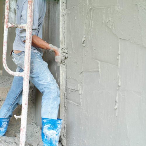 Worker plastering the cement on the wall by wooden trowel at the construction site